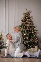 adult man and woman sit on the floor near the christmas tree and hug