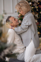 Fototapeta premium adult man and woman sit on the floor near the christmas tree and hug