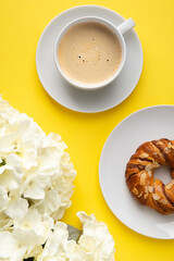 White cup of coffee and flowers on yellow background