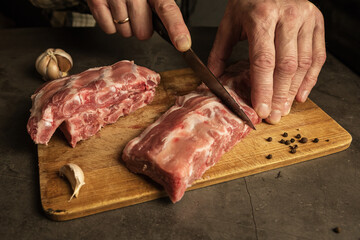 Men's hands cut fresh pork ribs. Cooking for frying with garlic, allspice on a wooden board, gray background.