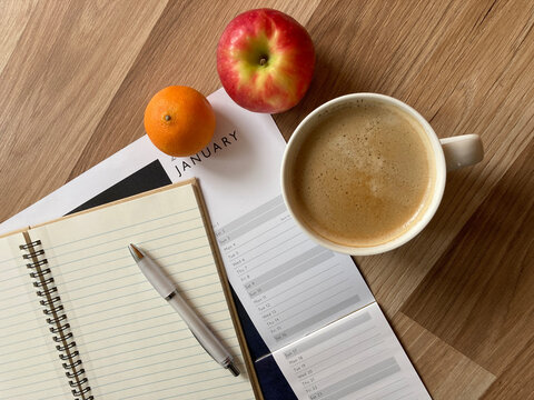 Workplace with calendar, notebook, pen, coffee and healthy fruit snacks on a desktop.