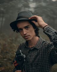 Obraz premium young man traveler in with a hat and a camera looking for adventure in a foggy forest