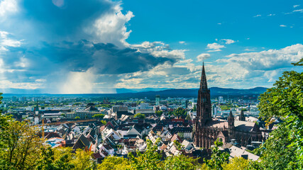 Fototapeta premium Germany, Freiburg im Breisgau, Rain and thunderstorm in summer above skyline of the city and muenster church, aerial view above