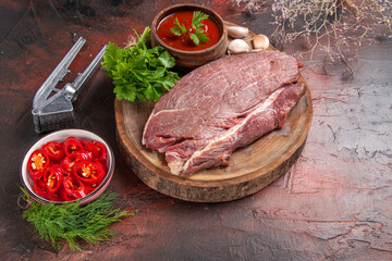 Side view of red meat on wooden tray and garlic green ketchup and chopped pepper on dark background