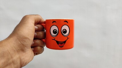 Human hand holding orange smiley coffee mug