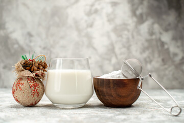 front view a glass of milk a bowl of powdered sugar with sieve and decorated pinecones on grey isolated background with copy space