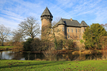 Fototapeta na wymiar Panoramic view over moat on medieval ancient old german water castle and defensive tower from 12th century with bare trees in winter against blue sky - Krefeld Linn, Germany
