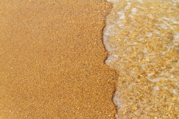 A sea wave with white foam runs over the yellow sand of the seashore.