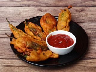 Mirchi pakora or Mirchi bhajji served with sauce, a famous midday snack in india, served over a rustic wooden background, selective focus