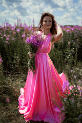 Smiling young woman with dark long hair holding the bouquet of pink flowers. Pink Ivan Tea or blooming Sally in the field