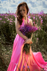 Smiling young woman with dark long hair holding the bouquet of pink flowers. Pink Ivan Tea or blooming Sally in the field