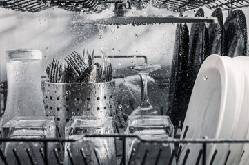 Transparent and black and white dishes as well as cutlery and glasses are washed in the dishwasher,...