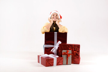 Happy pretty woman in red santa claus hat staying near the stack of gift christmas boxes isolated on the gray background