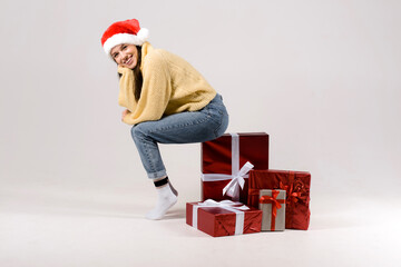 Woman sitting on the stack of gift christmas boxes isolated on gray background