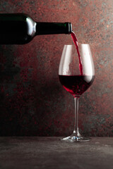 Red wine is poured from a bottle into a wine glass on rusty brown background.