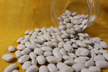 White dry beans in a jar lies spilled out on a yellow lemon background with a copy of the space