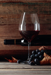 Red wine and a bunch of grapes on an old wooden table in the wine cellar.