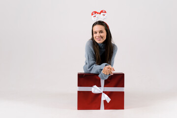 Happy excited woman in funny head hoop staying near the red big gift christmas box isolated on the gray background