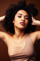 pretty young african american woman with curly hair posing cheerful gesturing on brown background, lifestyle people concept