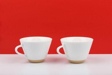 Two white ceramic coffee cups against red background on white glossy table with space for text. Concept of coffee break, refreshment and energy drinks