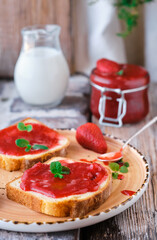 Sweet strawberry jam on toast close-up. Selective focus. The snack is decorated with mint leaves, vertical frame, close-up. Breakfast or lunch idea