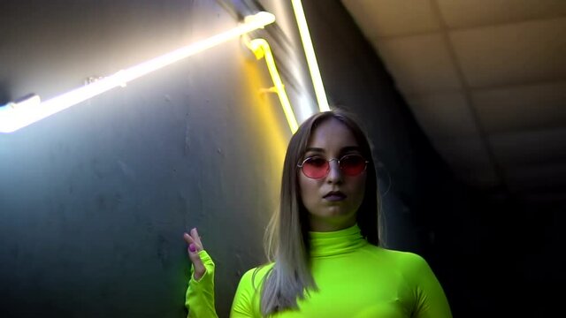 The girl unfolds and waves her hair. Glamor girl in glasses on the background of neon lamps