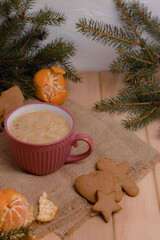Home Christmas comfort, pink cup with coffee next to a branch of a christmas tree with tangerine and gingerbread on a wooden table, christmas table with coffee, happy new year time