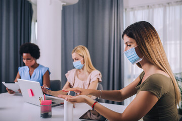 Fototapeta premium Female business colleagues with face masks working in the office