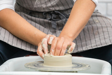 Potter woman's hands sculpt clay on a potter's wheel