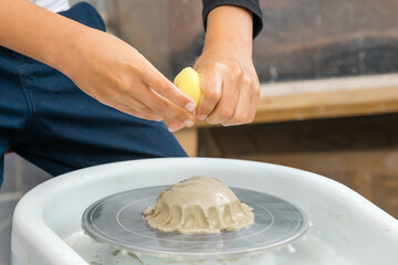 Boy pours water on clay on a potter's wheel