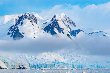 Snow-capped large mountains in Antarctica covered with gray clouds. Beautiful glacier
