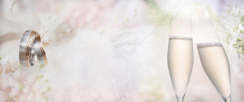 A couple of wedding rings with champagne on blurred delicate pink background. Horizontal close-up with space for text.