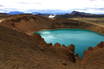 Downward view of the Viti crater lake with water vapor coming out of the Krafla geothermal power plant in the background (north of Iceland)