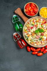 top view of bowl of vegetable salad with vegetables and oil vinegar bottles on side with free space for your text on dark grey background