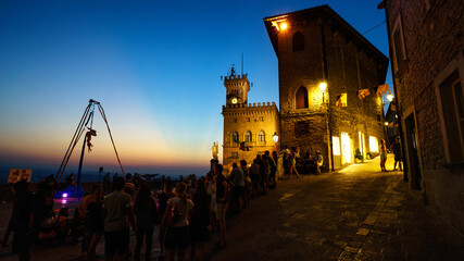 Fototapeta na wymiar Public Palace in San Marino at sunset. Crowd looking at street artist.