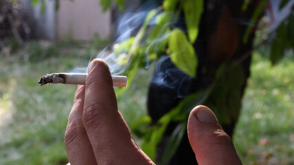 Gray smoke from smoldering cigarette in male fingers with dirty nails