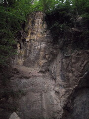 Dry from the summer heat forest waterfall. Dark rocks hang sheer between the lush forest.