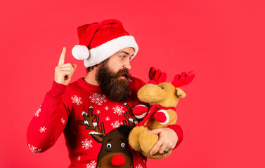 Lost in Christmas thoughts. Christmas party man with reindeer toy. happy guy await new year present. lets have fun. Santa Claus hipster. handsome man at Christmas. brutal bearded male red background