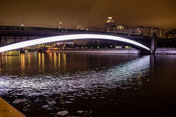 Fototapeta na wymiar evening winter cityscape with river bridge and illuminated buildings