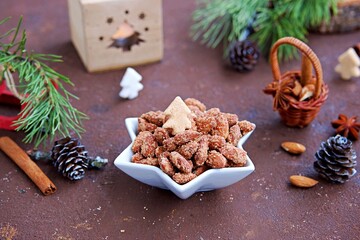 Homemade candied almonds in a white star bowl in a Christmas style on a brown concrete background. Christmas concept. Sweets recipes.
