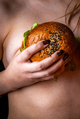 Young naked woman keep in her hands tasty burgers on black background