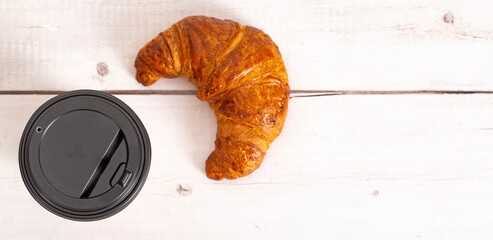 Paper cup of coffee and croissant on a light wooden background. Close-up. copy space. Free space for text. top view. Soft focus