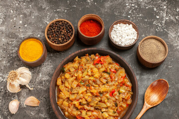 top view roasted eggplant salad in bowl wooden spoon different spices in bowls garlic on dark background