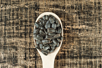 Fototapeta na wymiar Sunflower seeds in a wooden spoon on a yellow bamboo board. Nuts on a brown table.