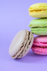 Group of french round cookies one on top of each other on purple background. Yellow, pink, green and brown almond cookies with fillings