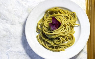 A dish of green spinach cooked spaghetti on a white plate.