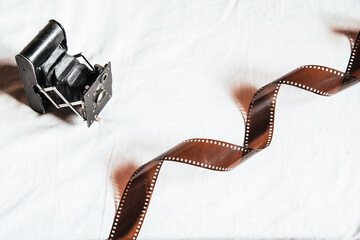 Una cámara antigua analógica al lado de una tira de película de 35mm sobre fondo blanco