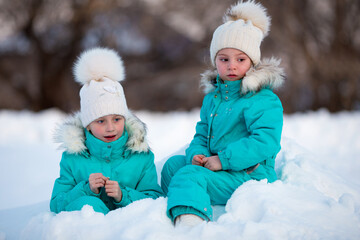 Fototapeta na wymiar Two funny little girls in identical clothes are having fun in a beautiful winter park. Cute kids playing in the snow. Winter activities for children.