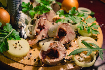 Sliced ​​mackerel, prepared for salting, with herbs, onions, spices and salt on a wooden board.