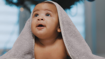 Adorable dark skin baby covered with towel having fun tummy time. High quality photo
